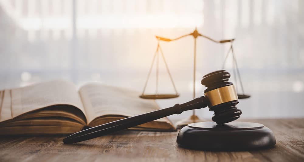 Image d’un marteau de juge posé sur un bureau, avec une balance de la justice et un livre ouvert en arrière‑plan, symbolisant le domaine juridique et les responsabilités du juriste d’entreprise.